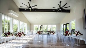 A spacious room with wooden flooring, clear plastic chairs, and floral centerpieces.