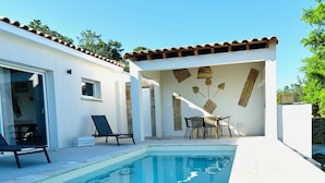 A modern outdoor pool area with a clear blue pool, lounge chairs, and a dining table. - Maison au Calme Avec Piscine (SAINT MICHEL D'EUZET)
