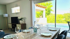 A dining area with a wooden table set for six, a TV, and a view of a swimming pool. - Maison au Calme Avec Piscine (SAINT MICHEL D'EUZET)