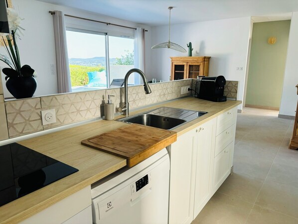 A modern kitchen with a large island, a built-in dishwasher, and a view through the window.