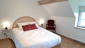 Un dormitorio con estructura de cama de madera, ropa de cama blanca, una silla roja y una ventana con luz natural.