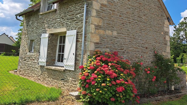 Una casa de piedra con techo inclinado, un pequeño balcón y un parterre lleno de flores rojas y amarillas.