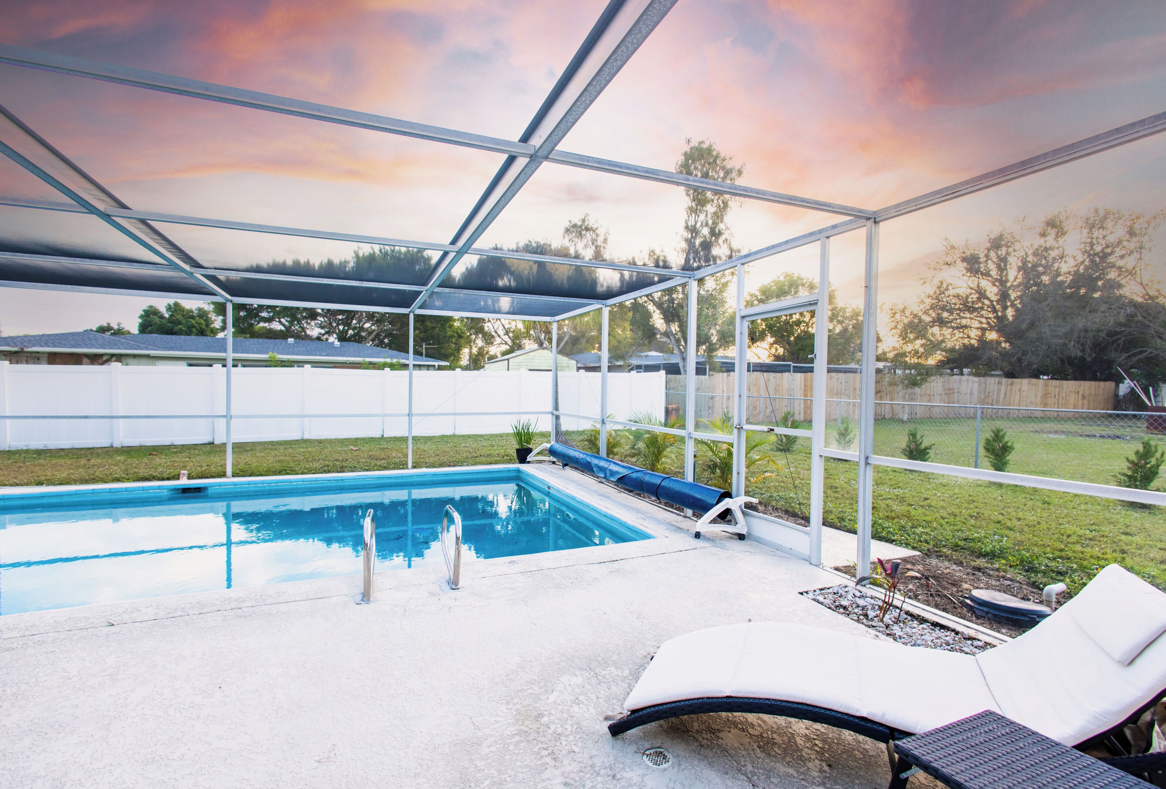A covered outdoor swimming pool with lounge chairs and a view of the backyard.