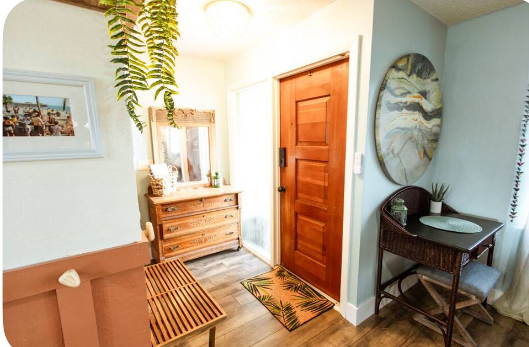 Un couloir avec un banc en bois, une commode en bois, une porte et un tableau accroché au mur.