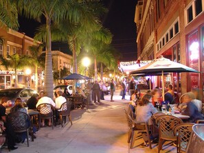An outdoor dining area with tables and chairs, palm trees, and a building with a sign. - Roze Family Villa- heated pool home near river district & waterfront dining! (North Fort Myers)