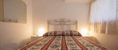 A bedroom with a bed, two bedside tables, a mirror, and an air conditioning unit.
