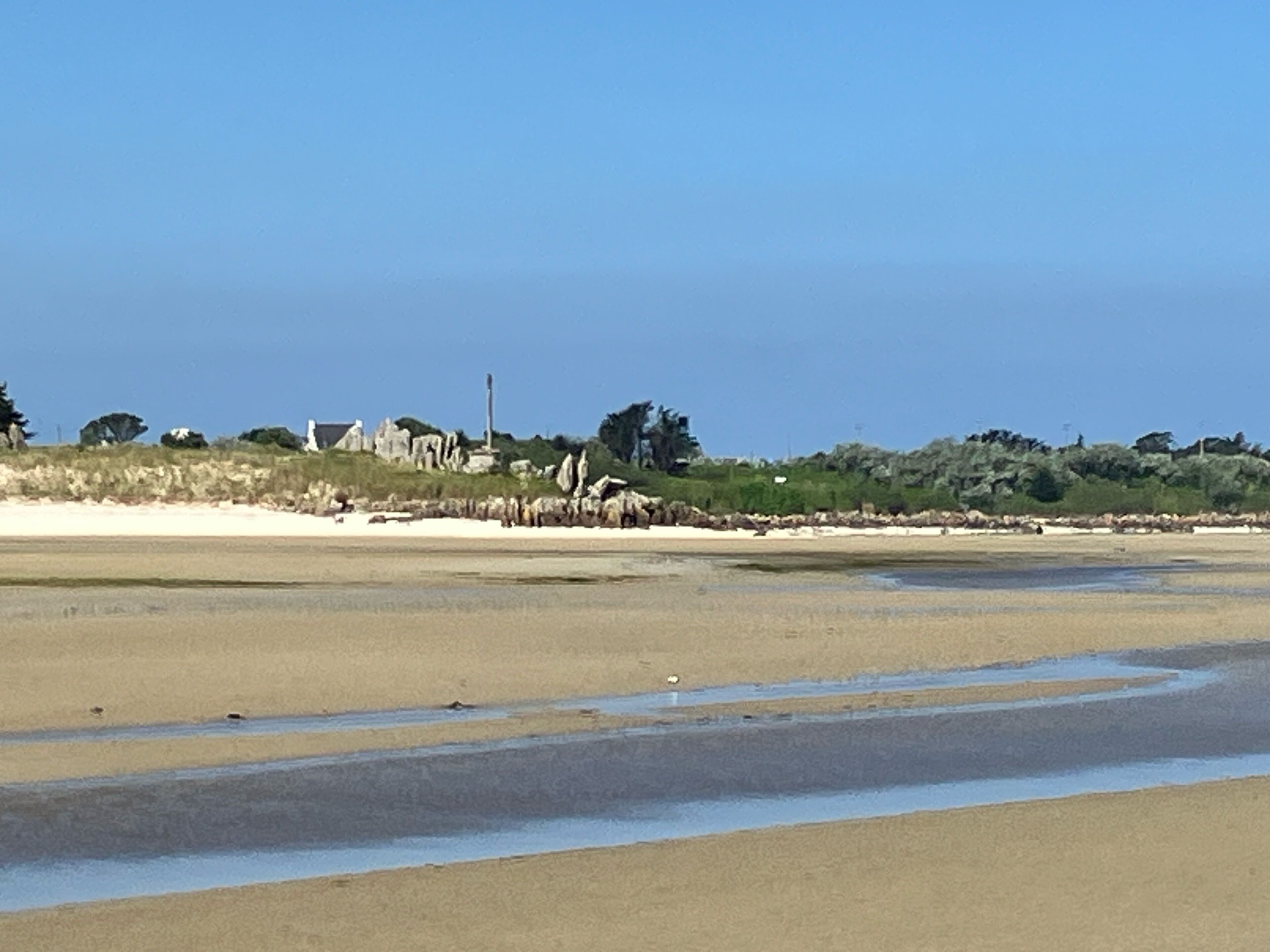 Ein Strand mit einem weiten Sandbereich und einem Felsen im Hintergrund.