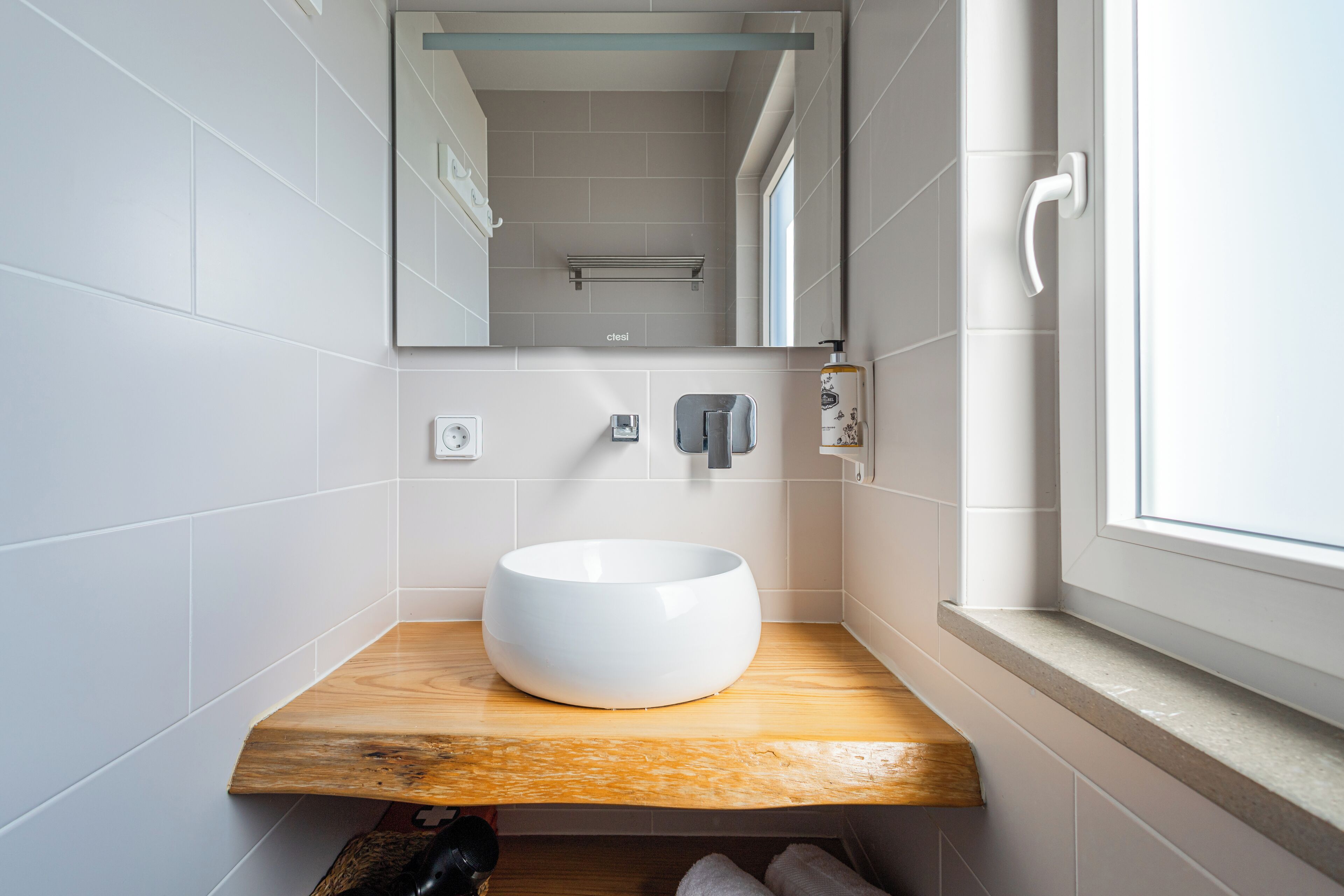 A modern bathroom with a white sink, wooden countertop, and a window.