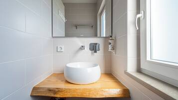 A modern bathroom with a white sink, wooden countertop, and a window.