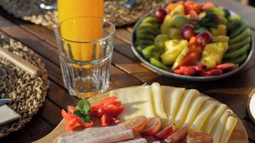 A wooden table with a plate of sliced meats, a glass of orange juice, and a bowl of fruit.