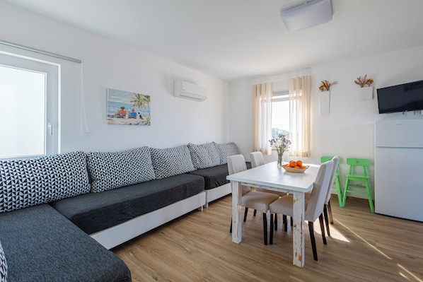 A modern living room with a sectional sofa, a dining table with chairs, a TV, and a kitchen area. - Monte do Cerro (Sines)