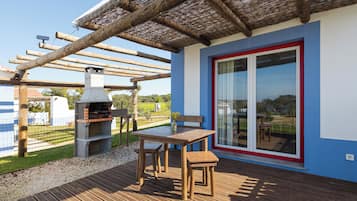 Un patio exterior con mesa y sillas de madera, una parrilla y una pérgola.