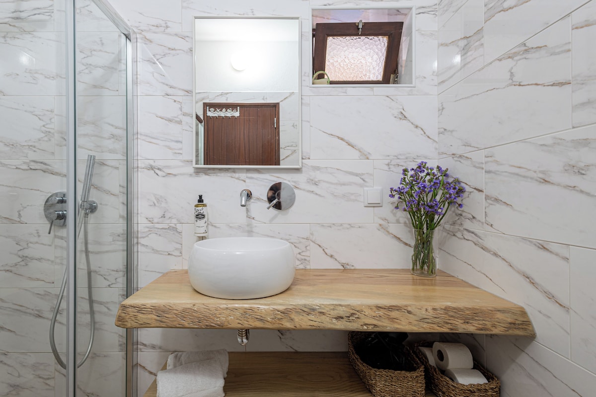 A bathroom with a glass shower enclosure, a wooden vanity, a white sink, and a mirror above it.