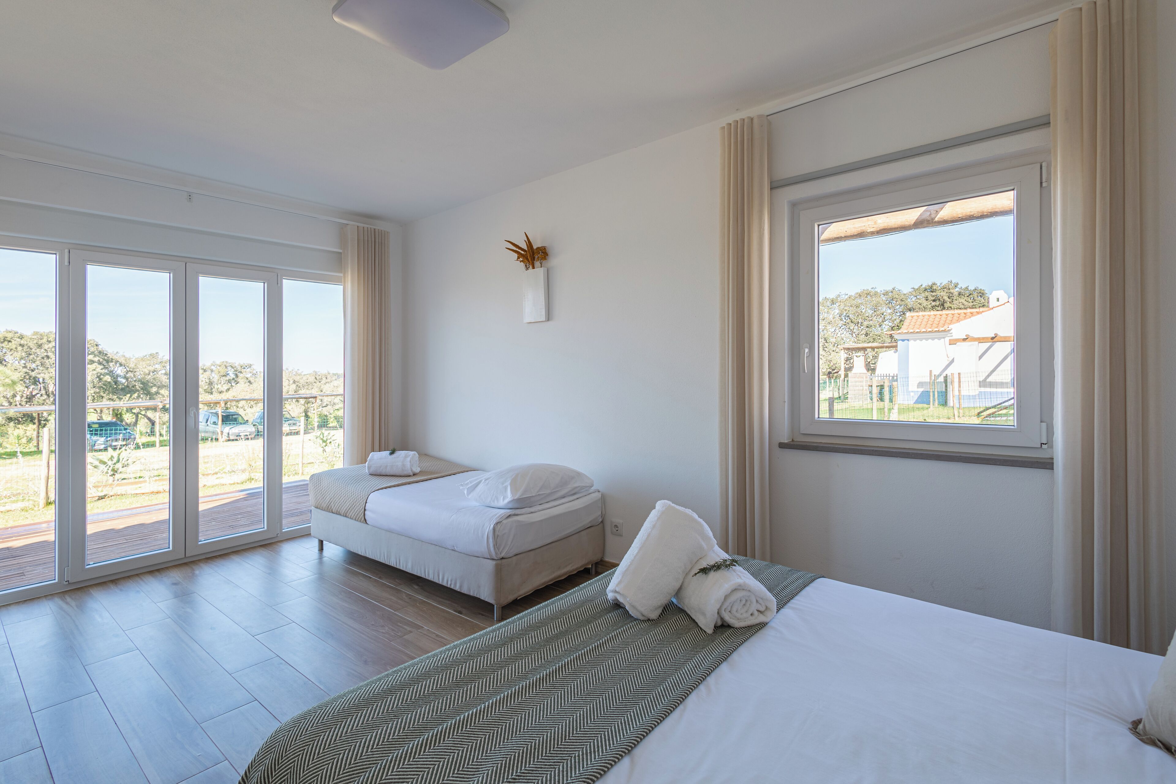 A hotel room with a large sliding glass door leading to an outdoor area, a bed with a green patterned bedspread, and a small bedside table with a lamp.