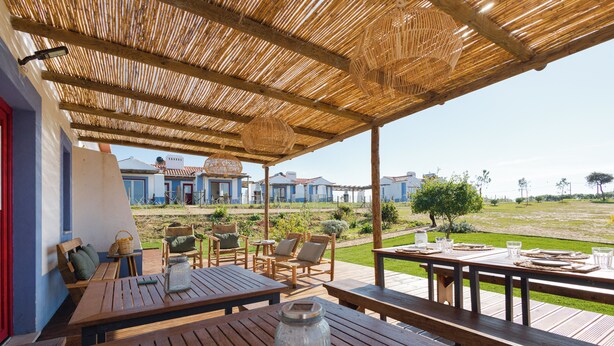 An outdoor patio with wooden tables and chairs, a wicker basket, and a clear view of the surrounding buildings.