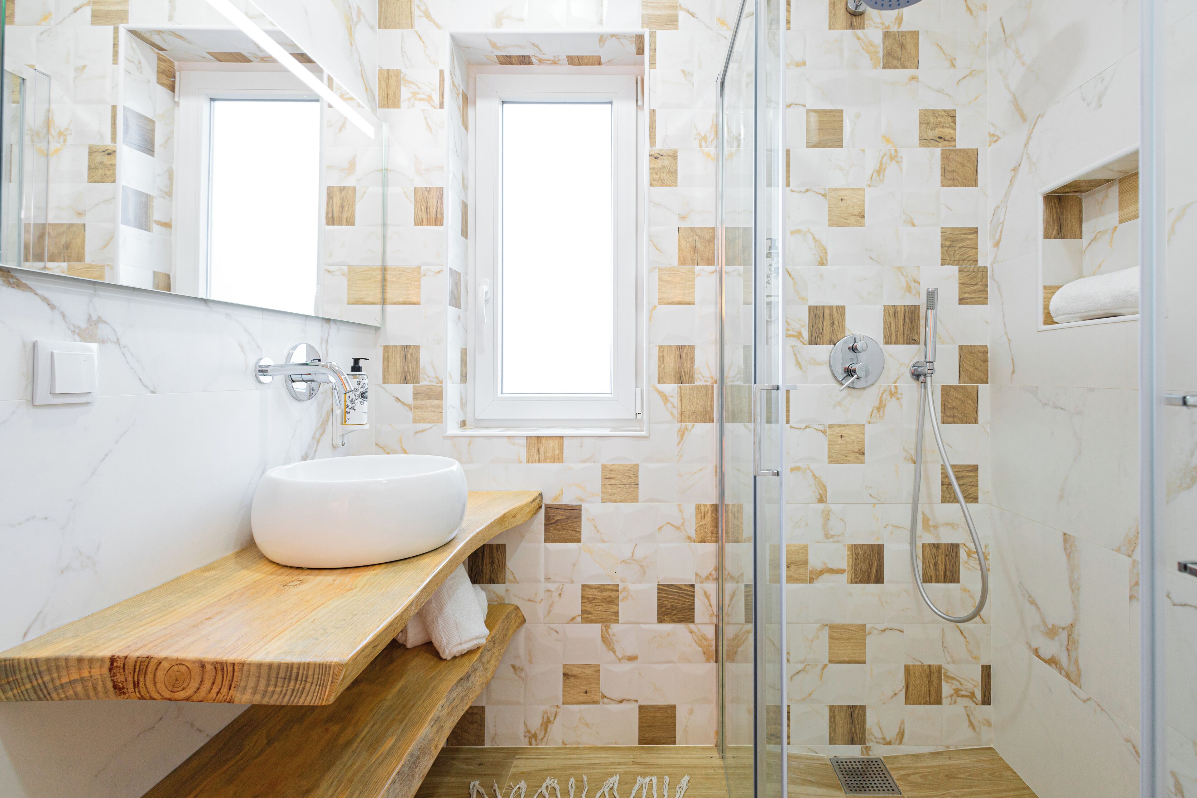 A modern bathroom with a marble vanity, a glass shower enclosure, and a wooden shelf.