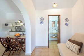 Una cocina moderna con una mesa de comedor y sillas, un microondas y un bol de fruta. Hay un sofá con un cojín en primer plano.