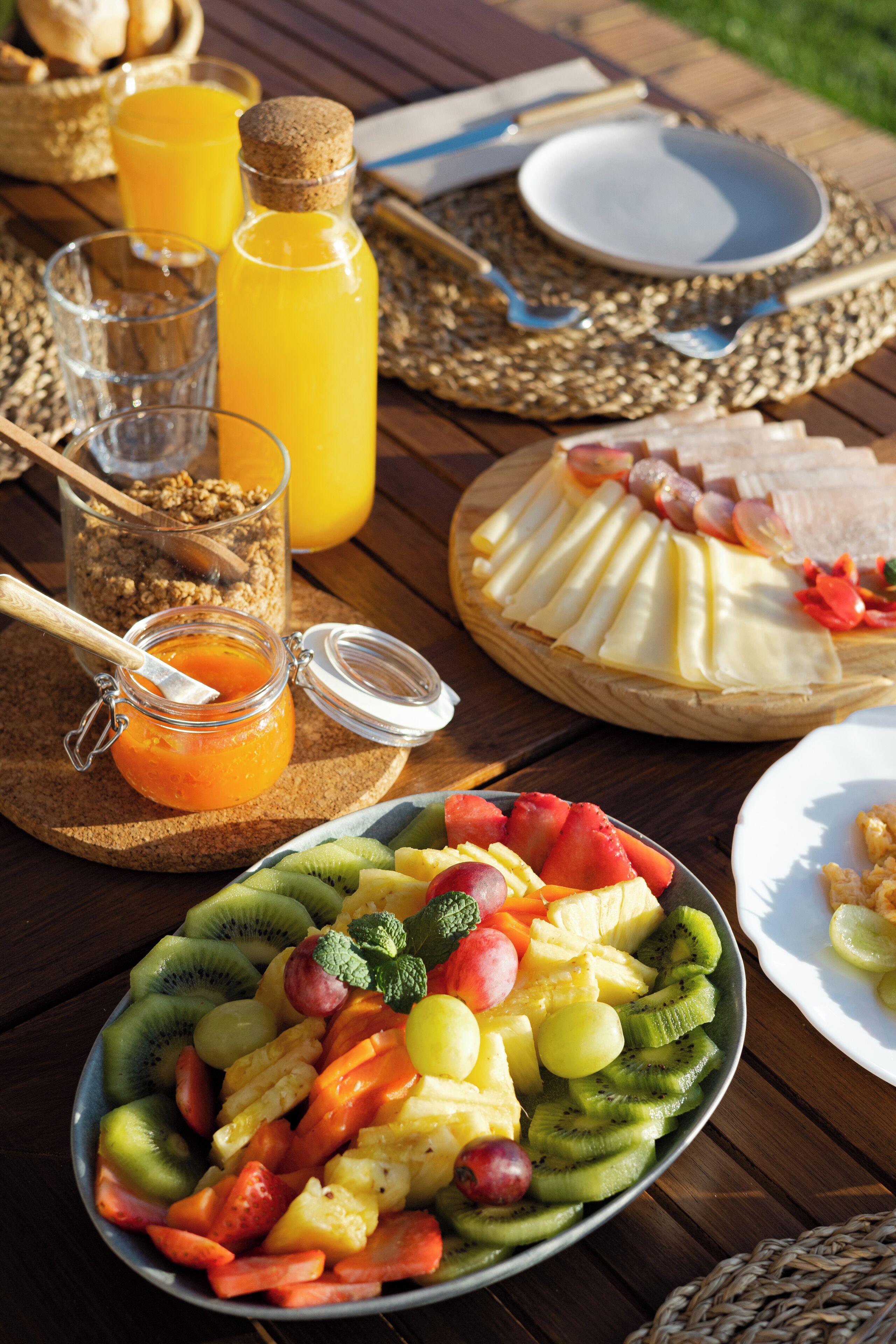 A breakfast setting with a fruit platter, a glass of orange juice, and a cheese board.