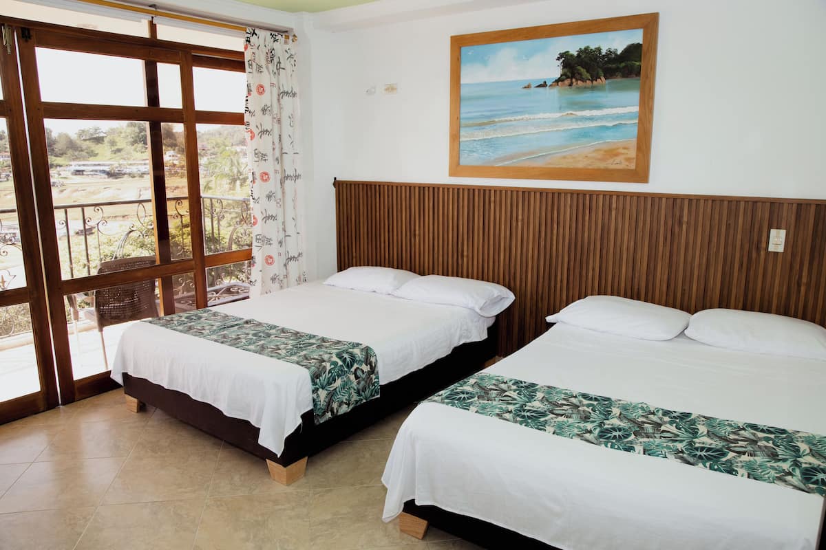Quarto com duas camas, uma janela grande com vista para o exterior e um quadro de uma praia na parede.