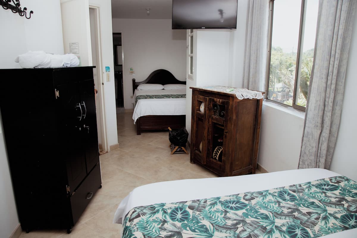 Quarto com cama, cómoda de madeira, guarda-roupa preto, televisão na parede e janela com cortinas.