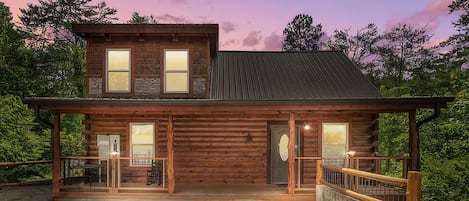 A two-story log cabin with a covered porch and a fenced front yard.