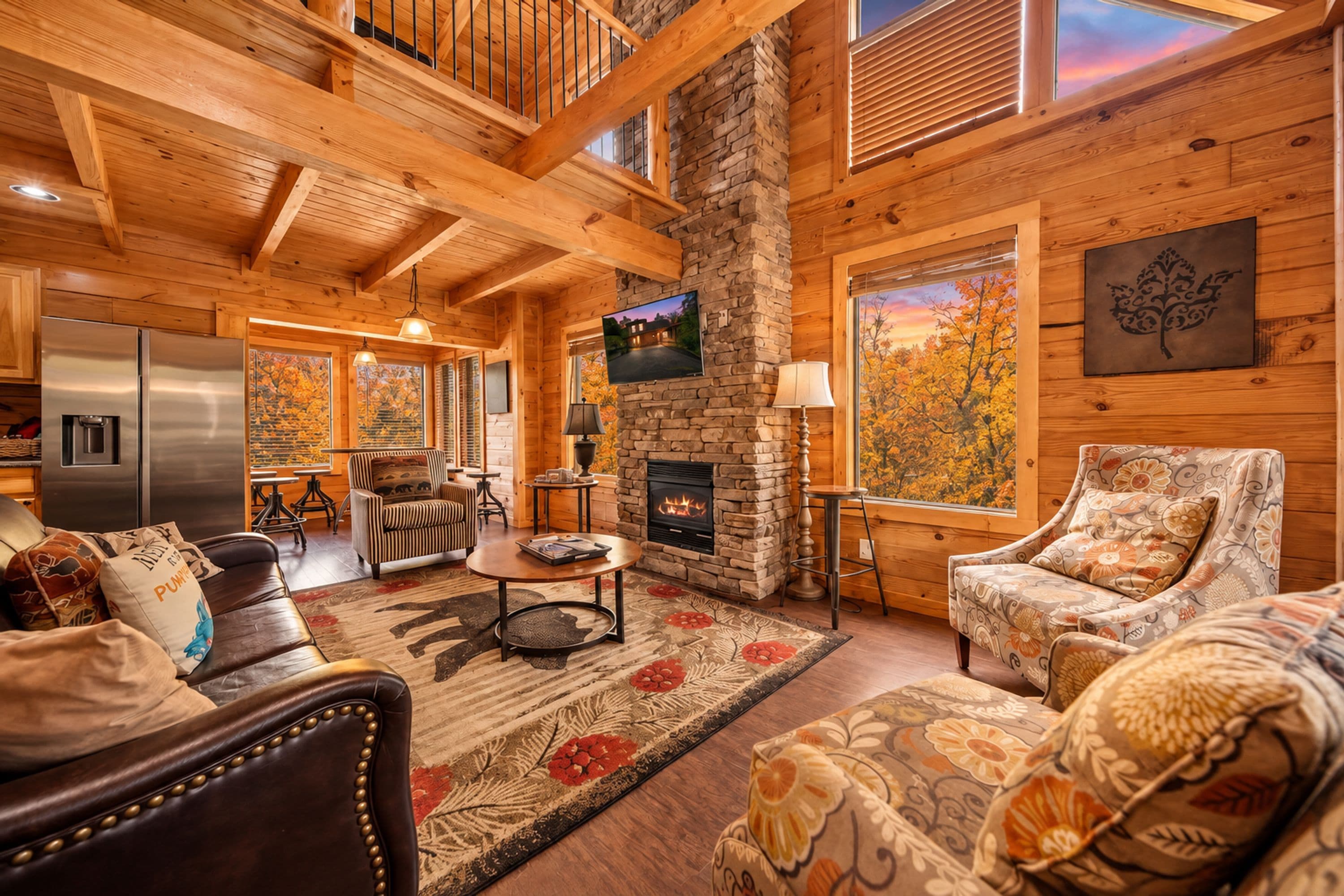 A cozy cabin interior with a stone fireplace, wooden walls, and a large window with a view of autumn foliage.