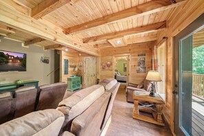A cozy cabin interior with a wooden ceiling, a large couch, a small table, and a television mounted on the wall. - Pigeon Forge I Hot tub I Theatre I Walk to Parkway (Pigeon Forge)