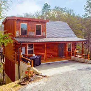 A two-story log cabin with a metal roof, a covered front porch, and a small front yard with a flower bed. - Pigeon Forge I Hot tub I Theatre I Walk to Parkway (Pigeon Forge)