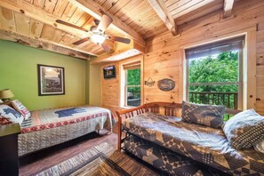 A cabin interior with a bed, a sofa, a ceiling fan, a window with a view of greenery, and a framed picture on the wall. - Pigeon Forge I Hot tub I Theatre I Walk to Parkway (Pigeon Forge)