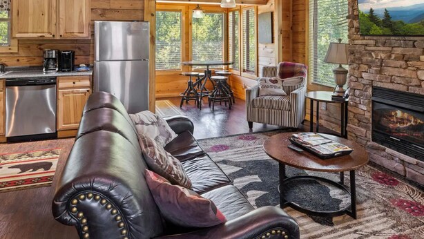 A spacious cabin interior with a kitchen, dining area, and living room, featuring wooden beams, large windows, and a fireplace. - Pigeon Forge I Hot tub I Theatre I Walk to Parkway (Pigeon Forge)