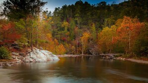 Une rivière paisible, avec des rochers et le feuillage automnal en arrière-plan.