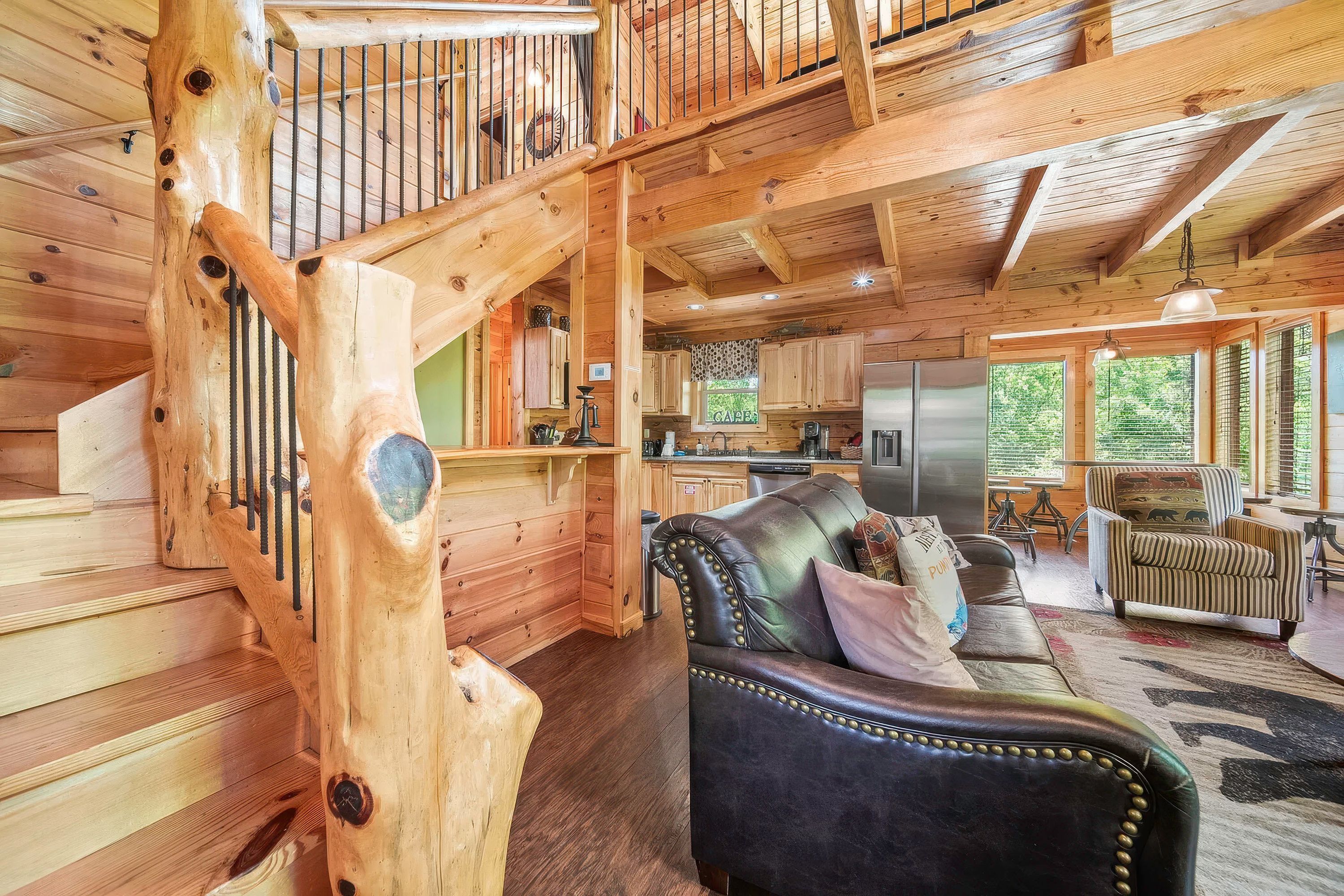 A wooden cabin interior with a staircase, a leather sofa, and a kitchen area.