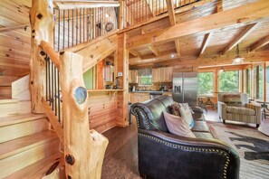 A wooden cabin interior with a staircase, a leather sofa, and a kitchen area. - Pigeon Forge I Hot tub I Theatre I Walk to Parkway (Pigeon Forge)