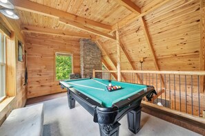 A wooden interior with a pool table, a stone wall, and a window overlooking greenery. - Pigeon Forge I Hot tub I Theatre I Walk to Parkway (Pigeon Forge)