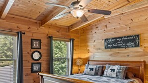 A wooden cabin bedroom with a bed, a ceiling fan, a bench, and a wall sign. - Pigeon Forge I Hot tub I Theatre I Walk to Parkway (Pigeon Forge)