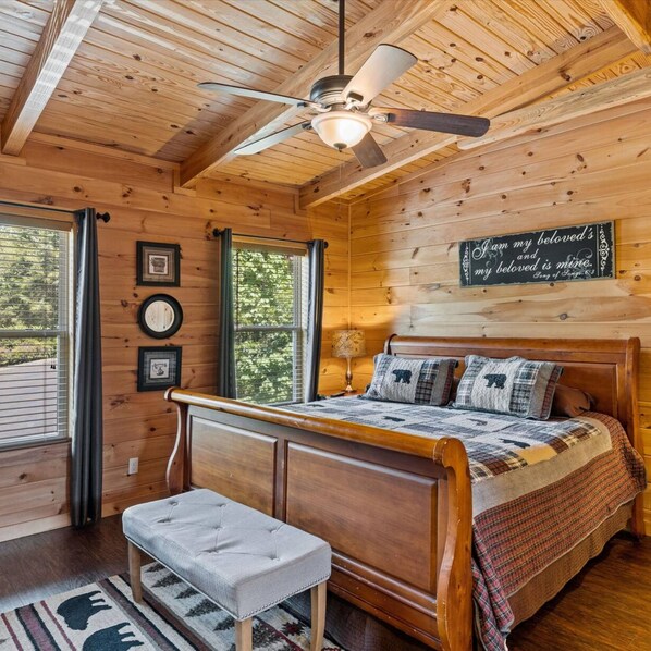 A wooden cabin bedroom with a bed, a ceiling fan, a bench, and a wall sign. - Pigeon Forge I Hot tub I Theatre I Walk to Parkway (Pigeon Forge)