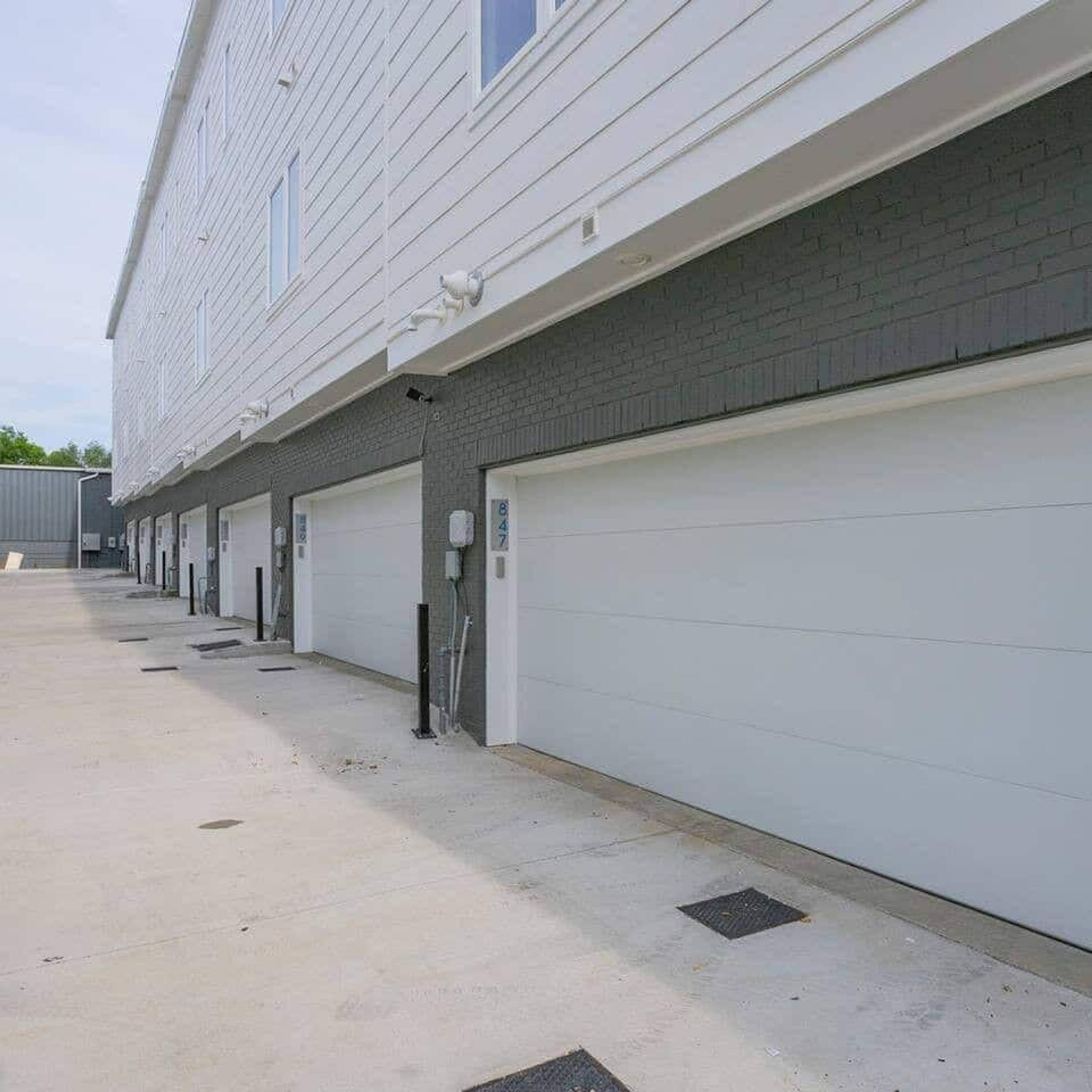 Hvide garageporte i række med en murstensfacade, en støbt indkørsel og en blå himmel.