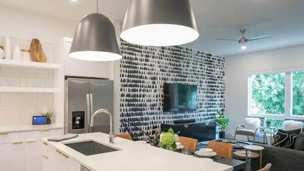 Eine moderne Küche mit Kochinsel, Edelstahlgeräten, Pendelleuchten und einer Wand mit Musterdesign.