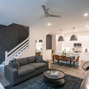 A modern living room with a grey sofa, a coffee table, and a staircase with white railings.