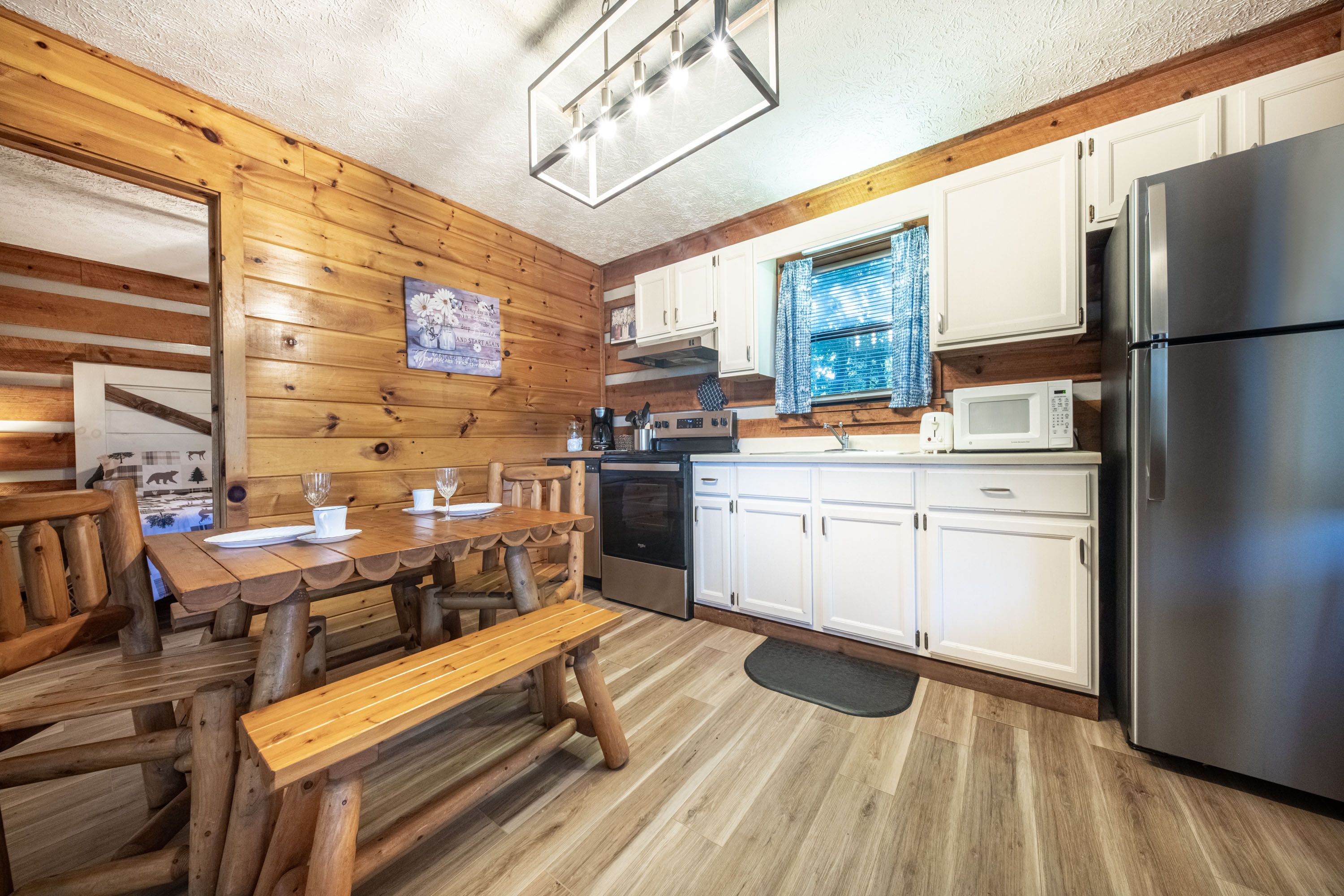 A wooden interior with a dining table, chairs, a bench, a refrigerator, a microwave, and cabinets.