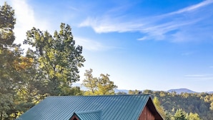 Une cabane en rondins surmontée d’un toit en métal, entourée d’une végétation luxuriante et avec des montagnes en arrière-plan.