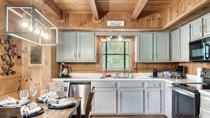 A wooden cabin-style kitchen with a dining area, featuring a sink, stove, and cabinets. - Minutes From Parkway I Private I Views I Hot tub (Pigeon Forge)