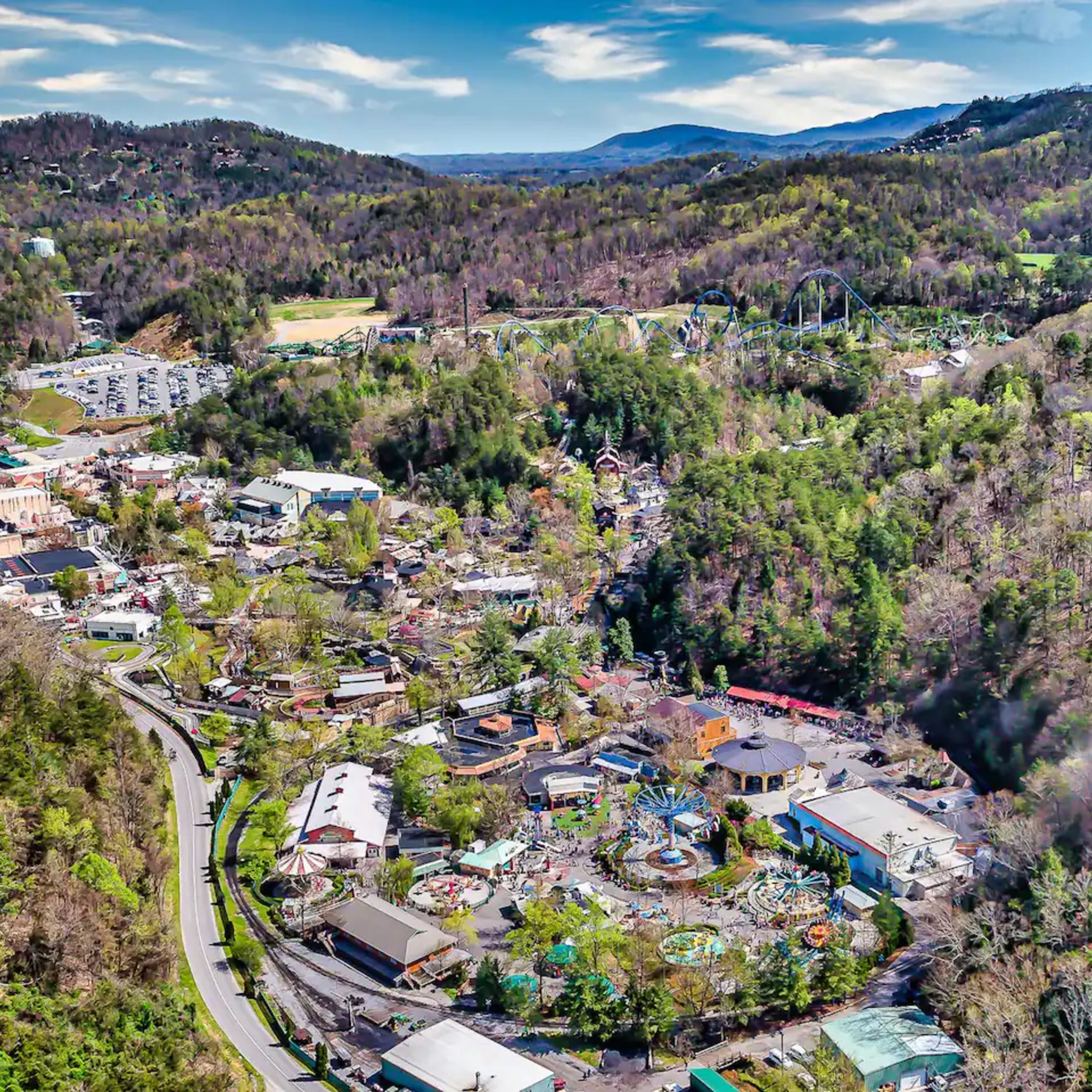 An aerial view of a town with a central park area, various buildings, and a road curving through the landscape.