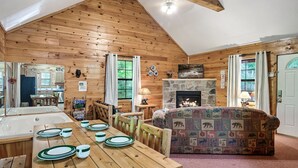 L’intérieur d’un chalet confortable, avec une salle à manger, une cheminée et un salon agrémenté d’un canapé à motifs.