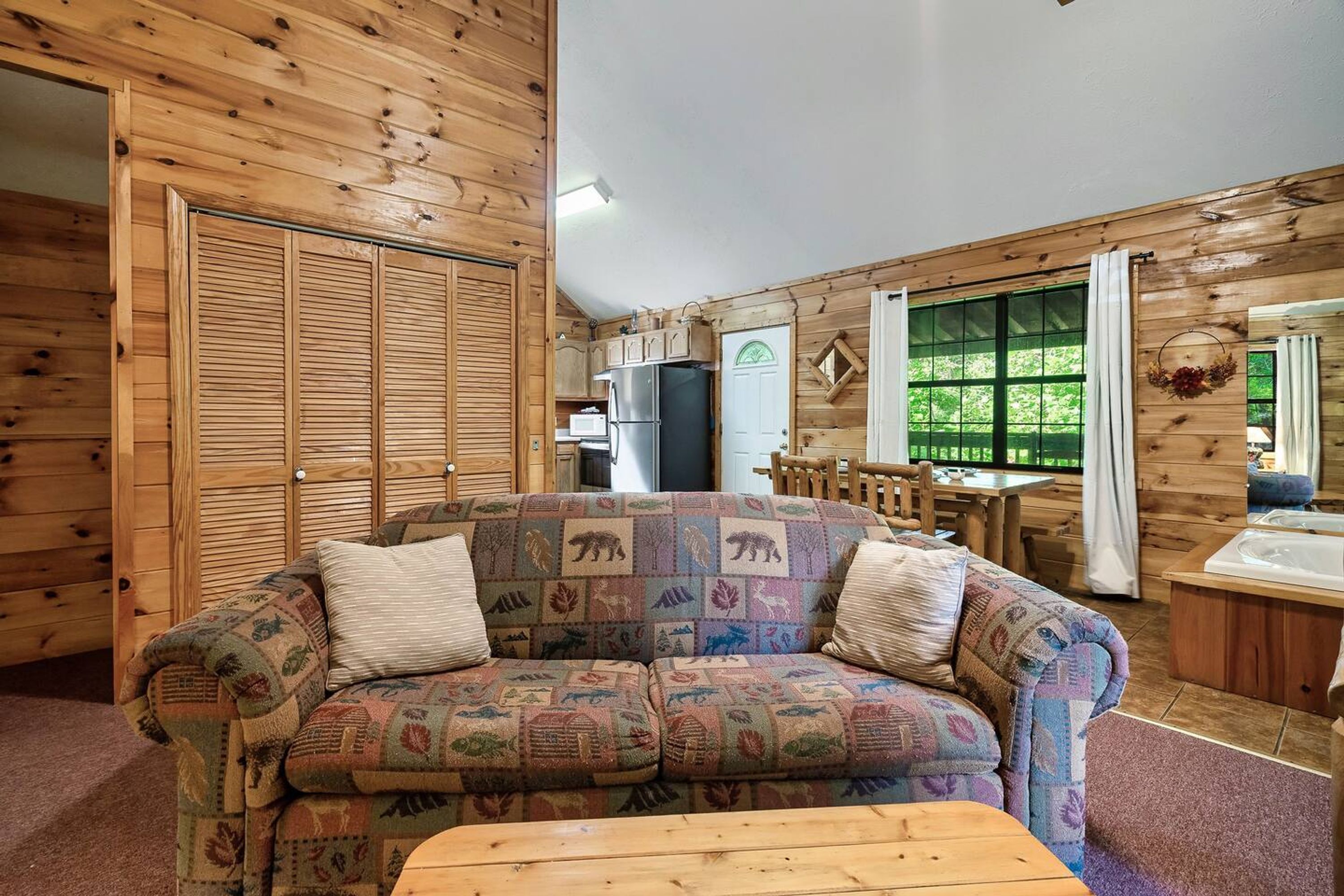 Un interior de cabaña acogedor, con detalles de madera, un sofá estampado, un comedor y un baño con bañera.