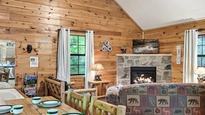 L’intérieur chaleureux d’un chalet avec une table à manger dressée pour quatre personnes, une cheminée et des murs en bois.