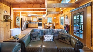 A cabin interior with a leather couch, wooden walls, a kitchen area, and a dining table. - Cozy Cabin Escape 7mins to Pigeon Forge Hot tub (Sevierville)