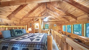 A log cabin bedroom with a bed, wooden walls, a ceiling fan, a window with a view, and a small table with a lamp. - Cozy Cabin Escape 7mins to Pigeon Forge Hot tub (Sevierville)
