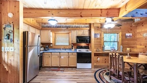 Het interieur van een houten chalet met een keuken, inclusief een koelkast, fornuis, magnetron en houten keukenkastjes.