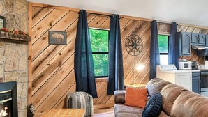 A cozy living room with a stone fireplace, wooden walls, a leather sofa, and a dining table.